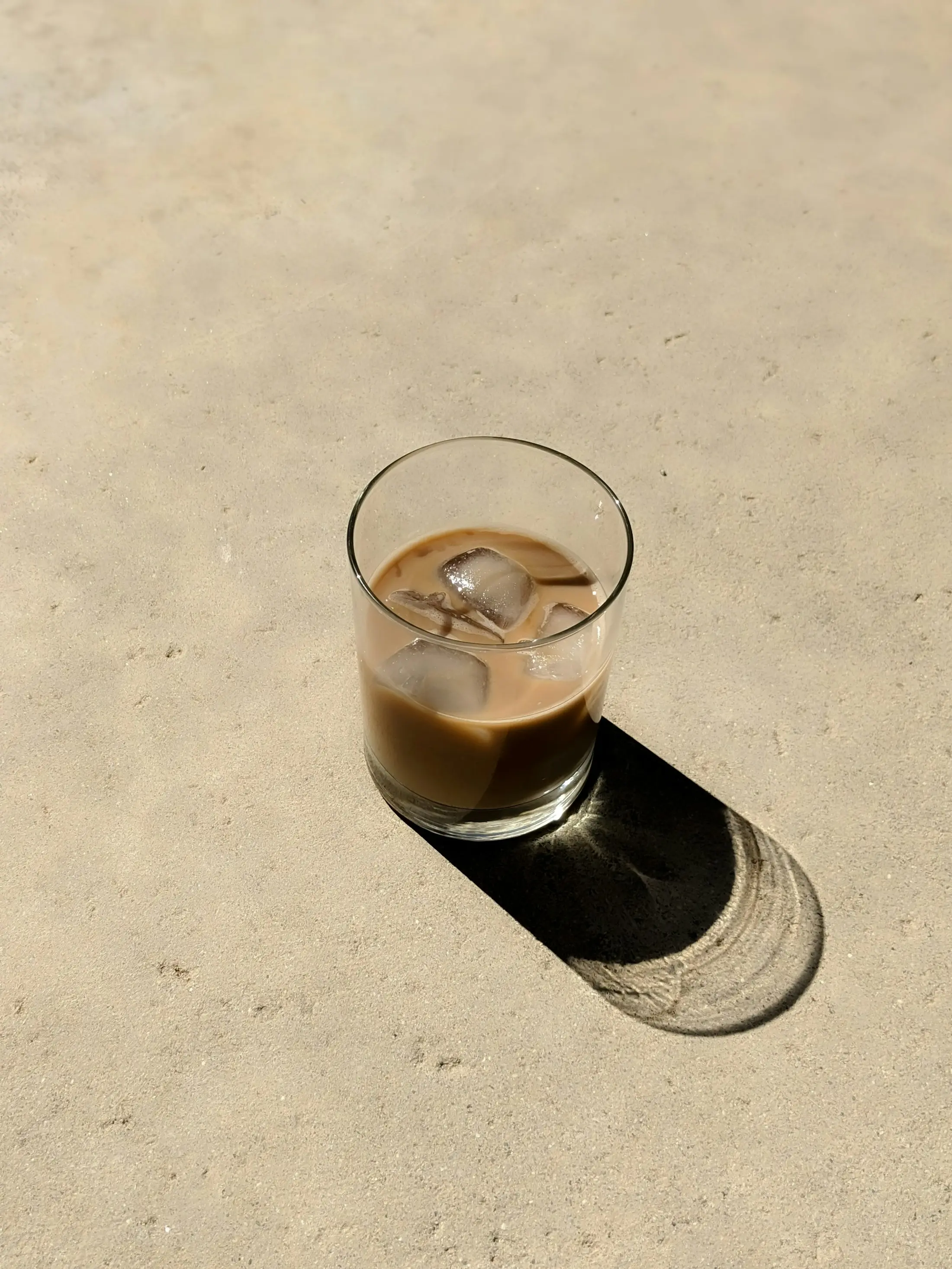كوب قهوة زجاجي تحت شمس الرياض وظله ممتد على الحجر